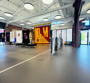 Sideway view of commercial dark grey sustainable resin floor with railway tracks in a light grey. Banner and t-shirts hanging in the background